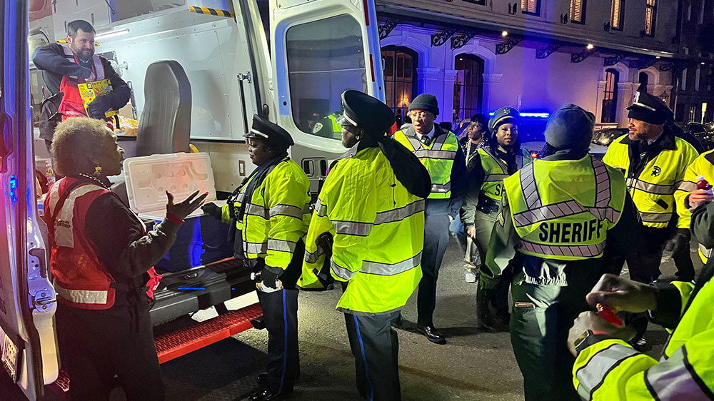 Red Cross volunteers in the back of a Red Cross van handing out snacks and drinks to police officers and mardi gras parade.