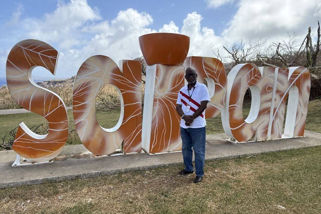 Dr. Levon LeBan stands in front of Saipan sign during his 3-week deployment to support the communities impacted by Typhoon Sinlaku.