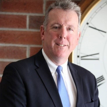 man in black blazer smiling, whitre shirt and blue tie