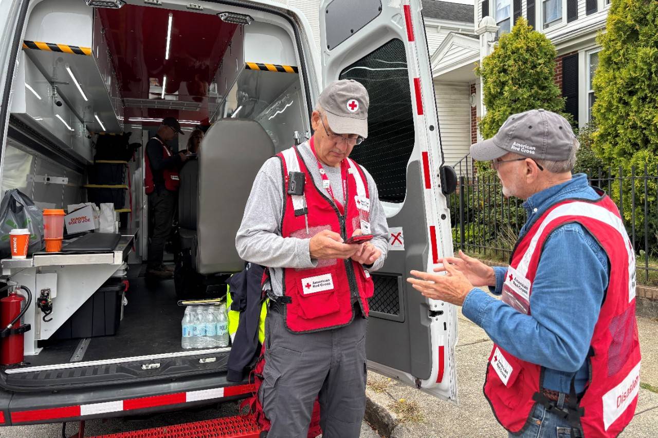 Two Red Cross volunteers stand outside emergency response vehicle