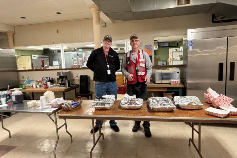 Two Red Cross volunteers stand behind table with food