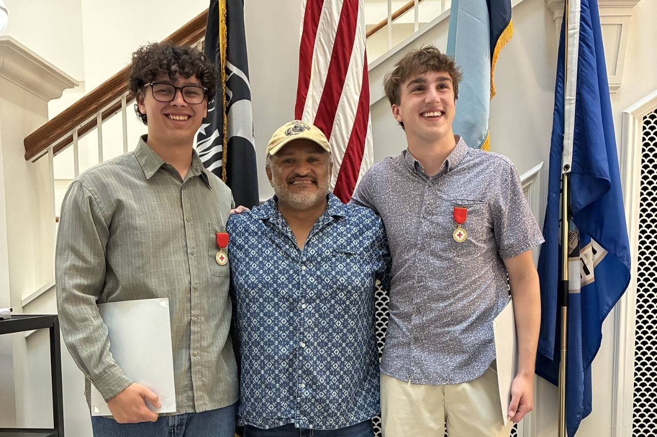 Man stands between two teenage boys in front of flags