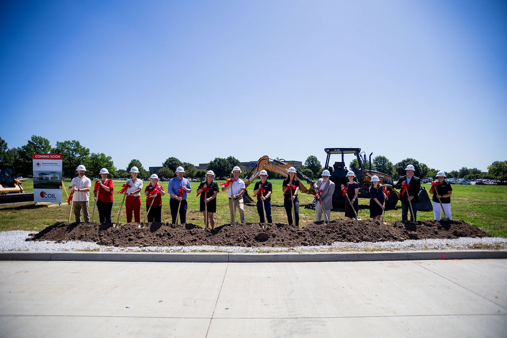 group of people in helmets shovelling dirt at grounding breaking event