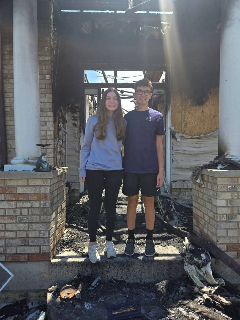 Two teens stand on front porch of home after it has burned