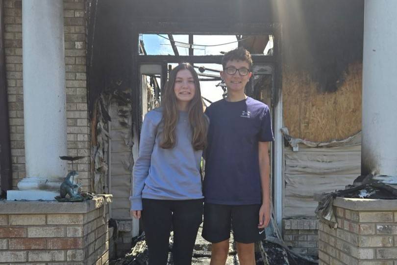 Two teens stand on porch of home that has been burned