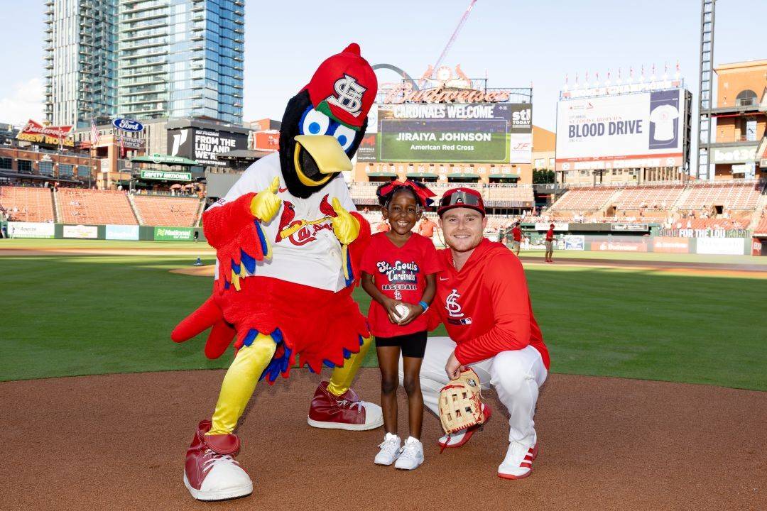Young girl stands on baseball field with baseball player and mascot