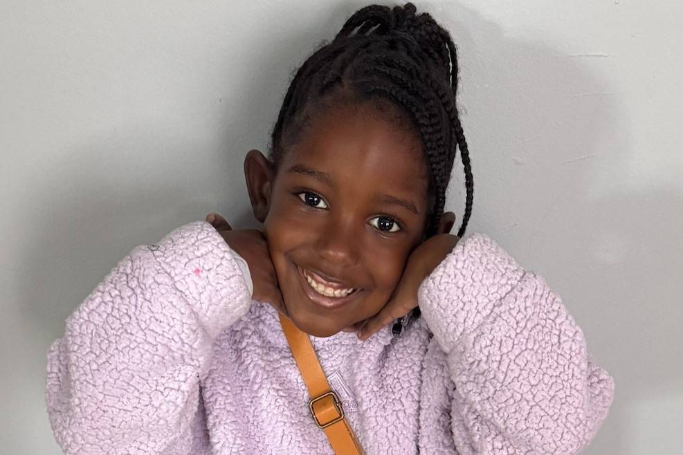 Young girl in pink sweatshirt smiles while tucking hands under her chin