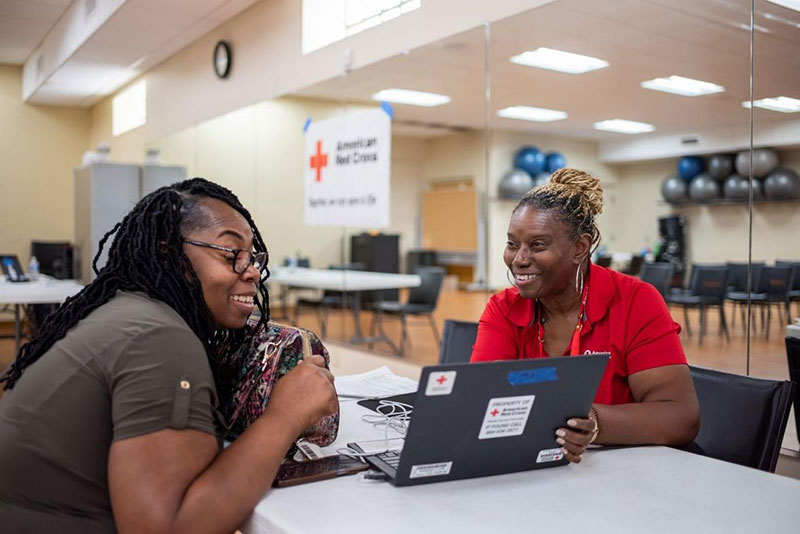 Jacqueline Robinson being helped by Red Cross volunteer looking at laptop