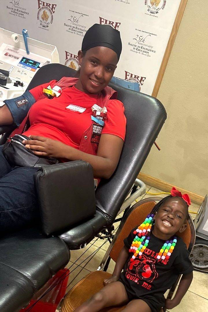 Young girl sits next to woman who is donating blood