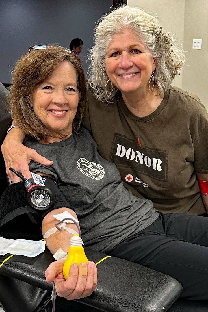 Woman puts arm around another woman who is donating blood