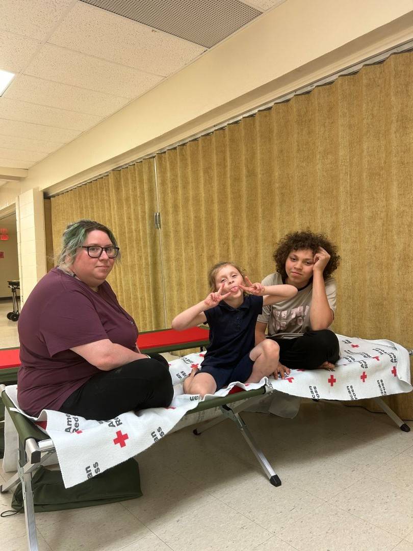 Woman sits on Red Cross cot with two young children
