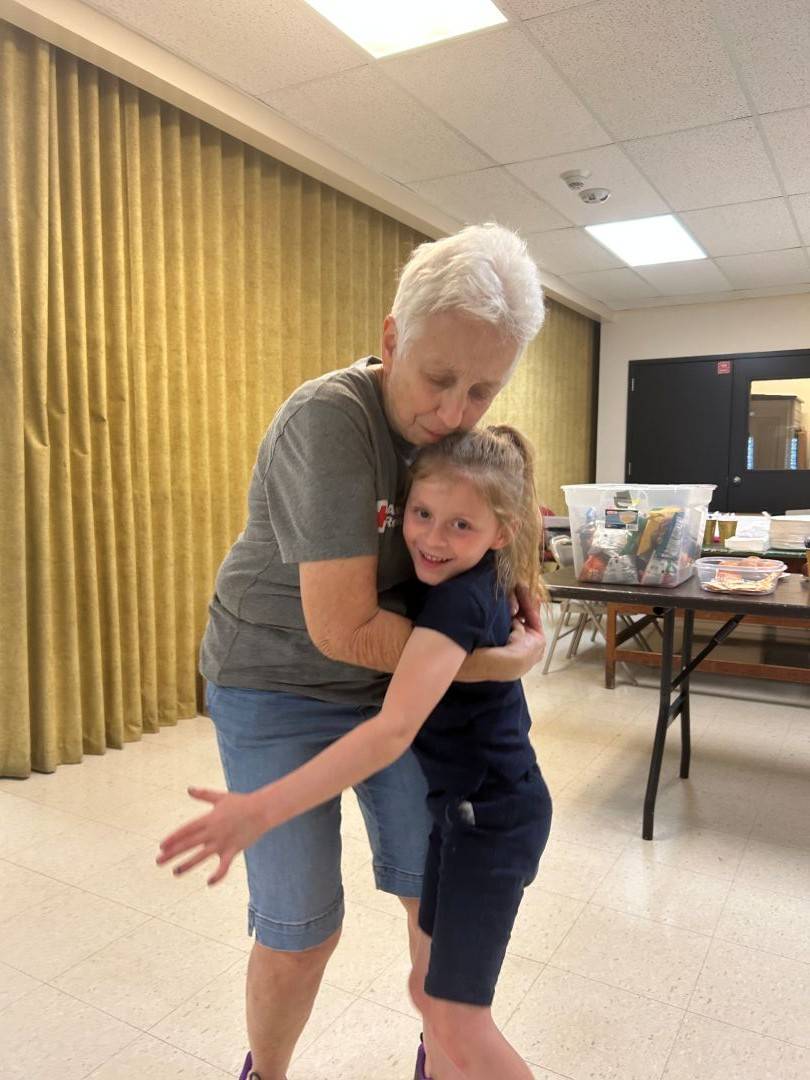 Woman in Red Cross shirt hugs young girl