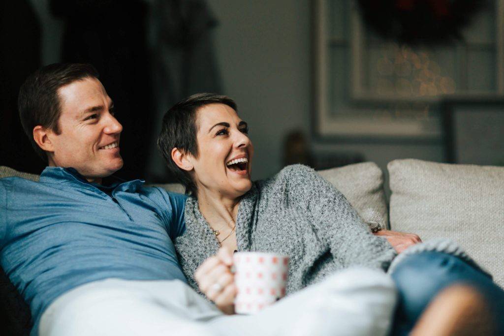 Man and woman snuggle together on couch while laughing