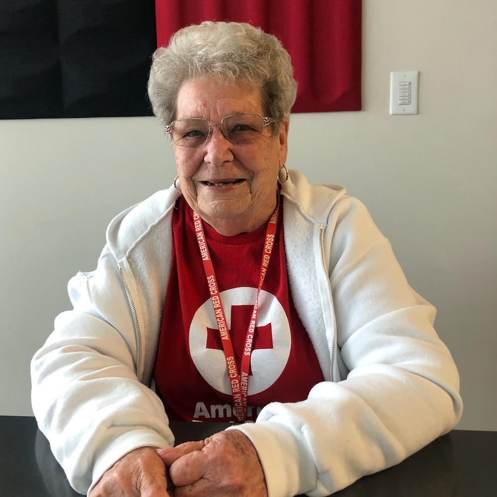 Phyllis Losack in Red Cross tee shirt sitting at a table
