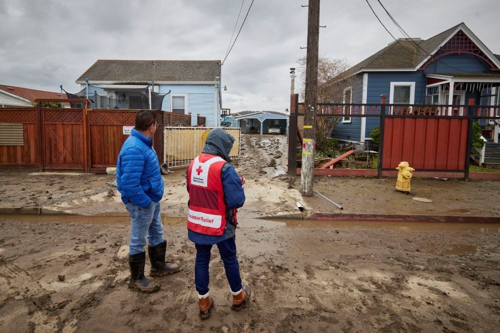 red cross volunteers standing surveying damaged home