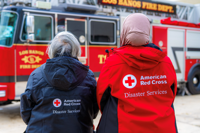 Two Red Cross volunteer standing next to a fire truck.