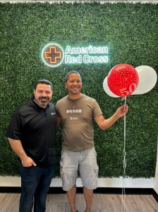 Rodrigo holding a red ballon next to a friend in frot of a "American Red Cross" sign