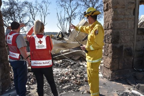 firefighter pointing to destroyed home to two red cross volunteers
