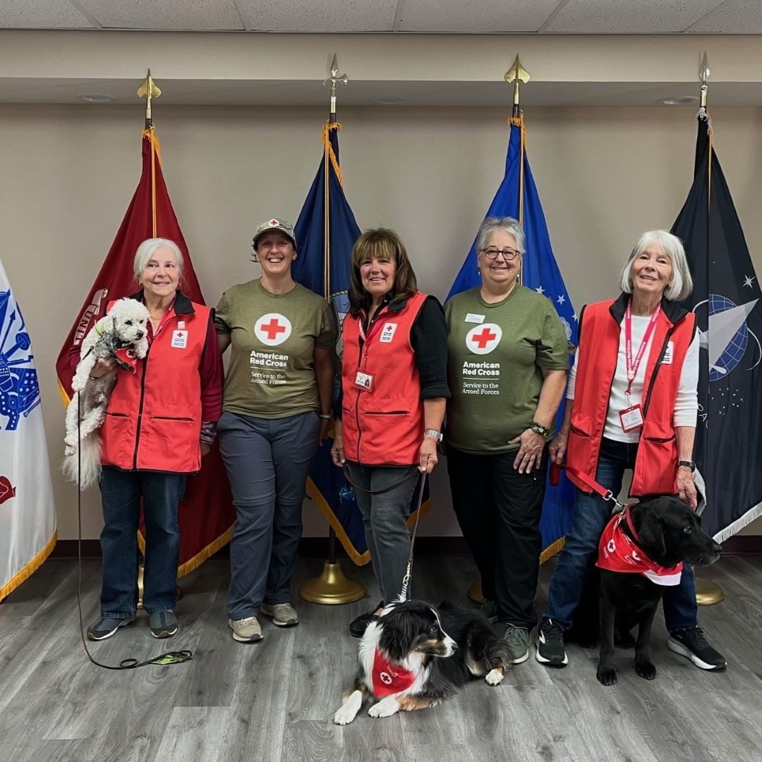 red cross volunteers and therapy dogs stand in front of flags