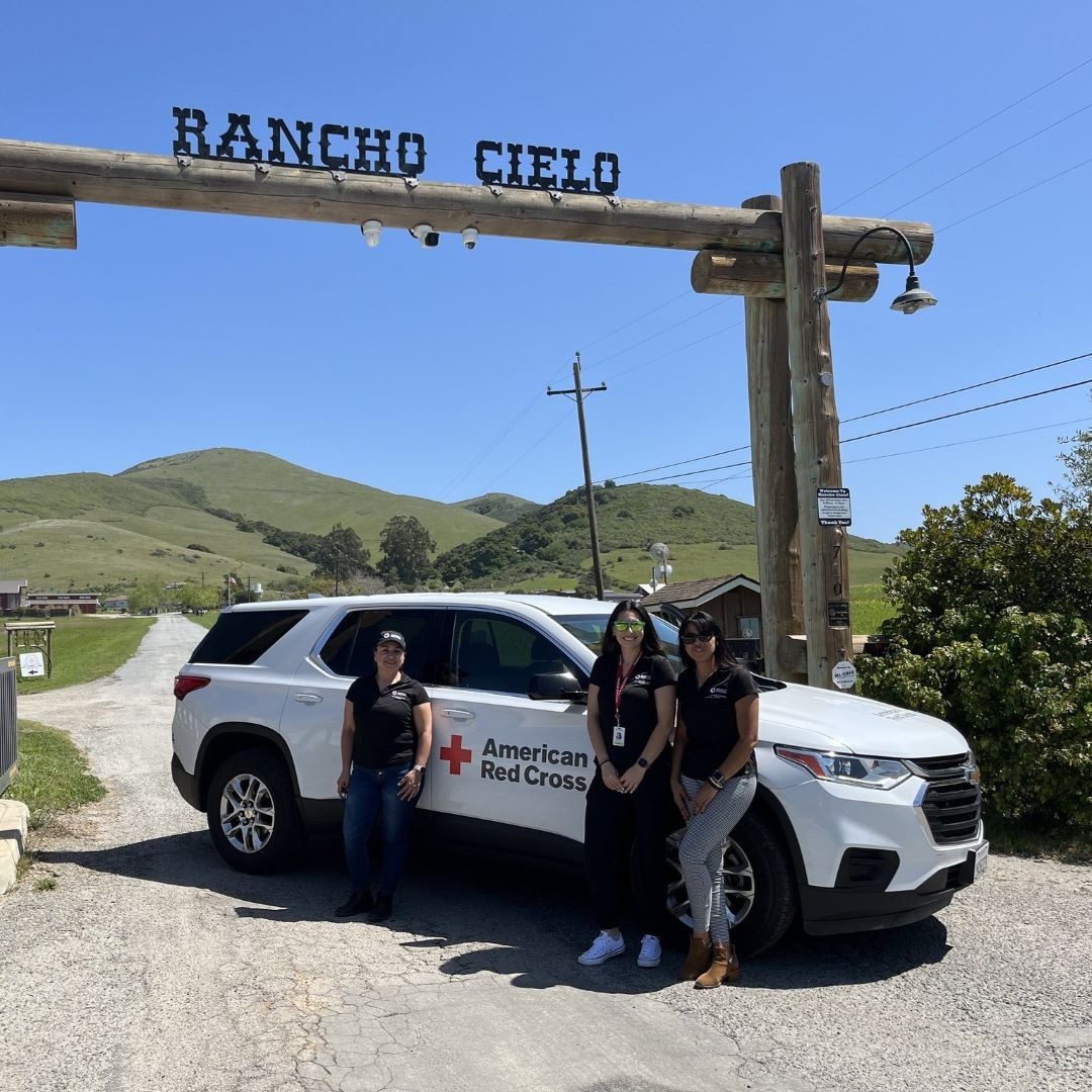 volunteers stand in front of red cross car at a ranch