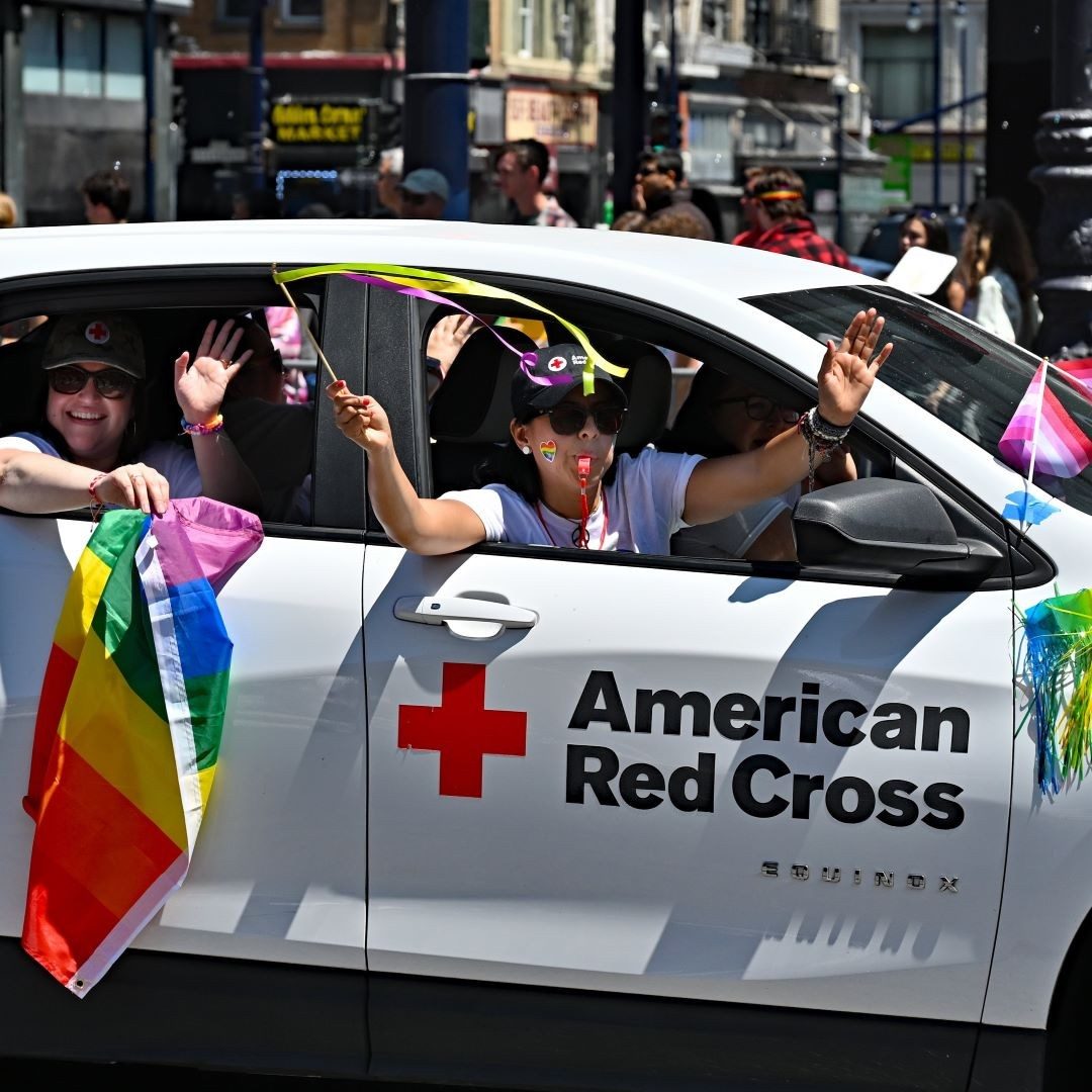 volunteers in red cross car waving pride flags