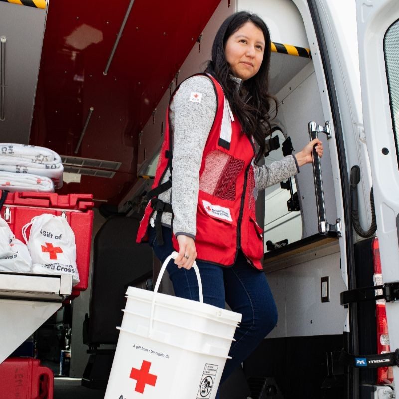 red crossvolnteer holding bucket leaving disaster response vehicle.