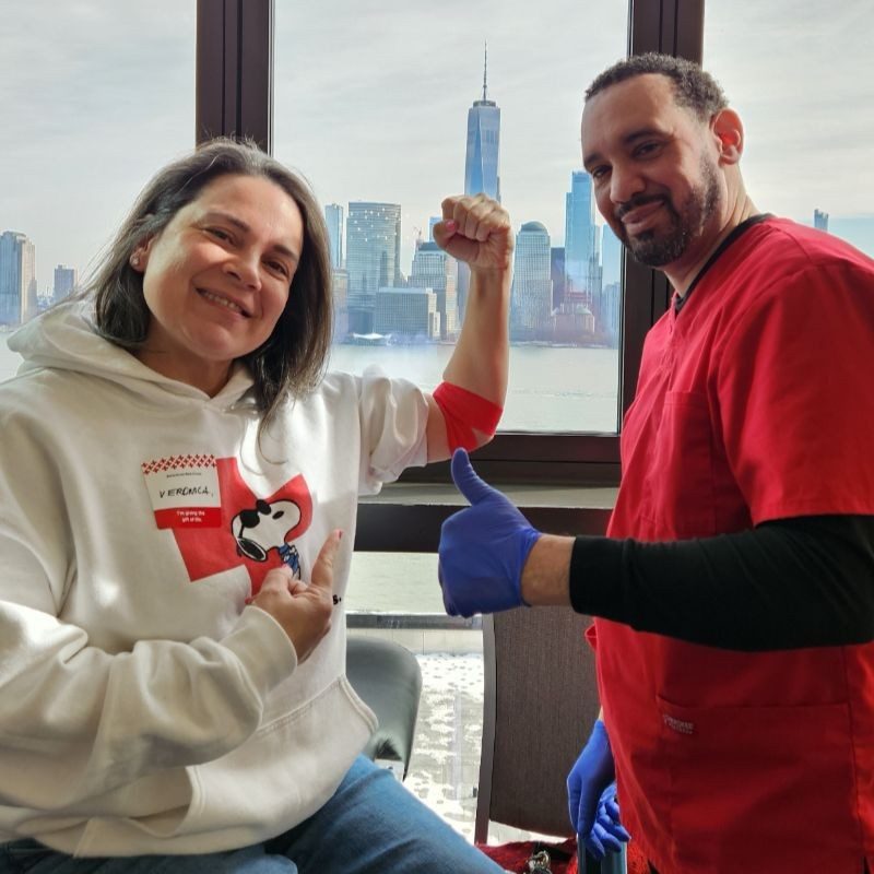 Red Cross blood donor holding up arm up next to a Phlebotomist