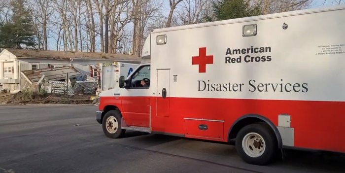 Red Cross emergency vehicle driving past destroyed homes