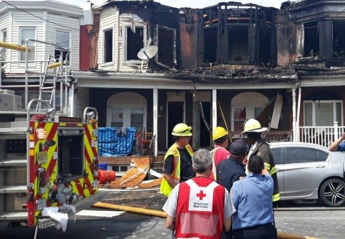 firefighters and red cross volunteers standing in front of a burnt home