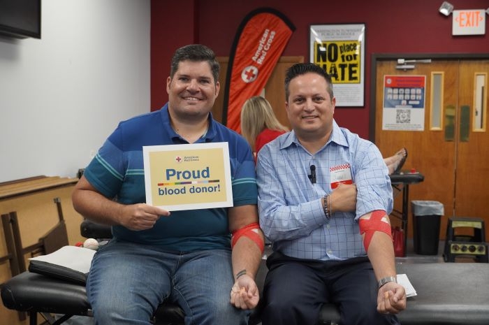 Matt and Jim giving blood holing a red cross proud sign 