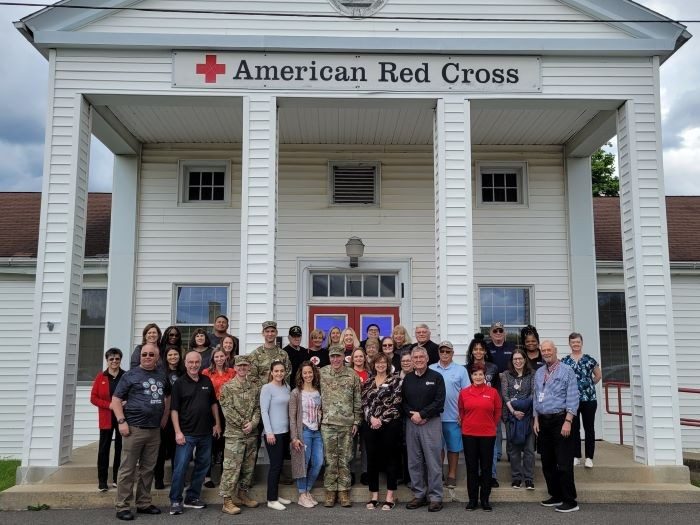 a group of people including miliatry members in uniform standing in front of a red cross building 