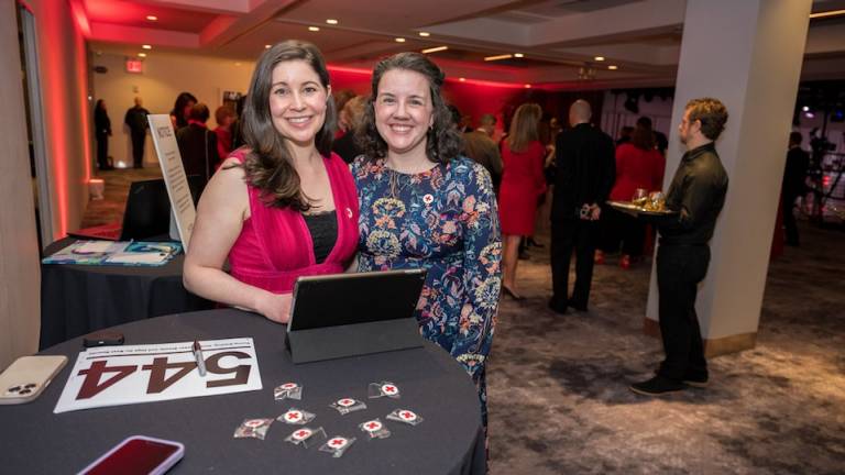 Two women and a table with a labtop and Red Cross pins on the table.