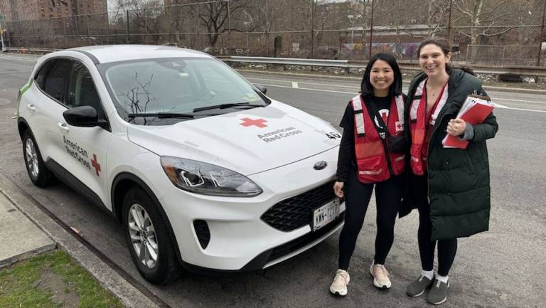 Two women in Red Cross red vests standing in front of a Red Cross vehicle.