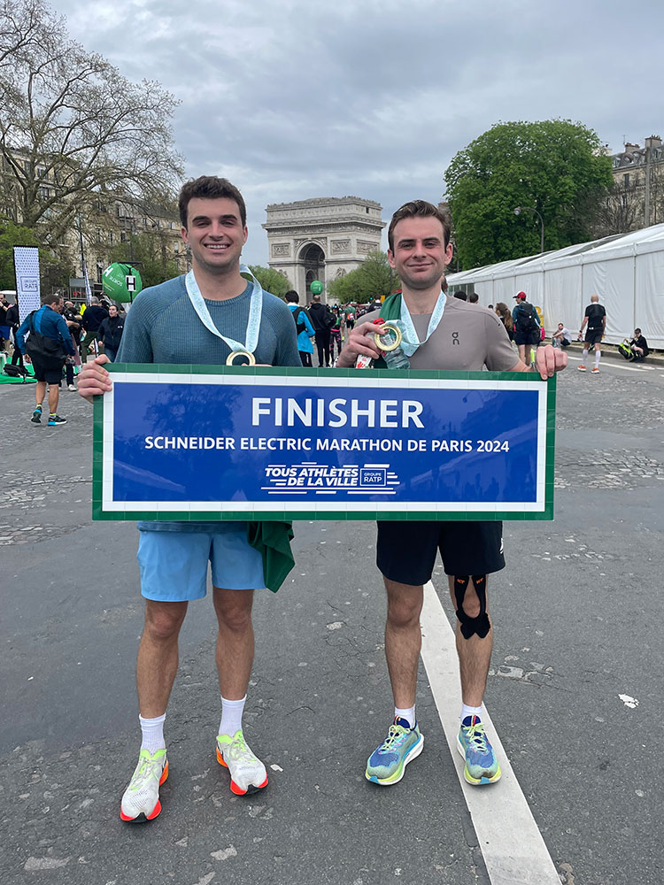 Emmet Coyle and another person at a marathon holding a sign and their medals.