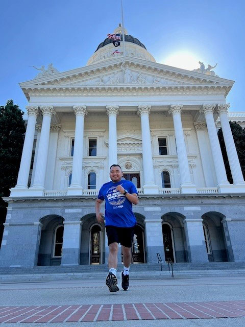 Fidel Gomez, wearing running gear, in front of a large white building.