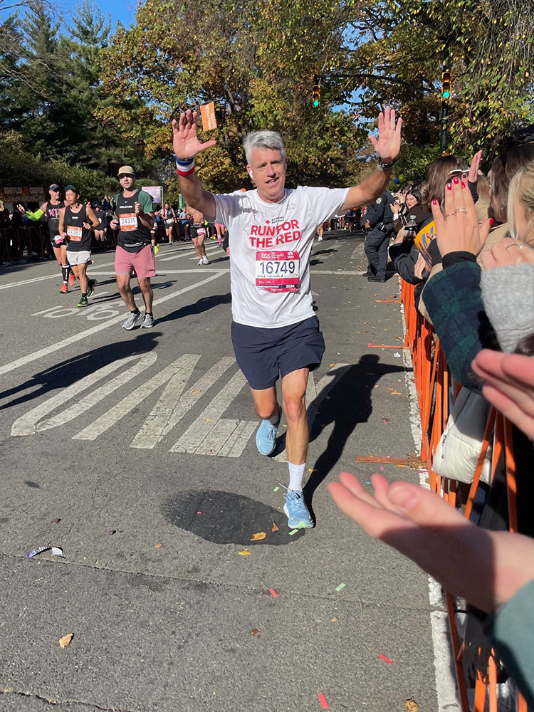 John Coyle, with his hands raised, running in a marathon and passing by onlookers on the side of the road.