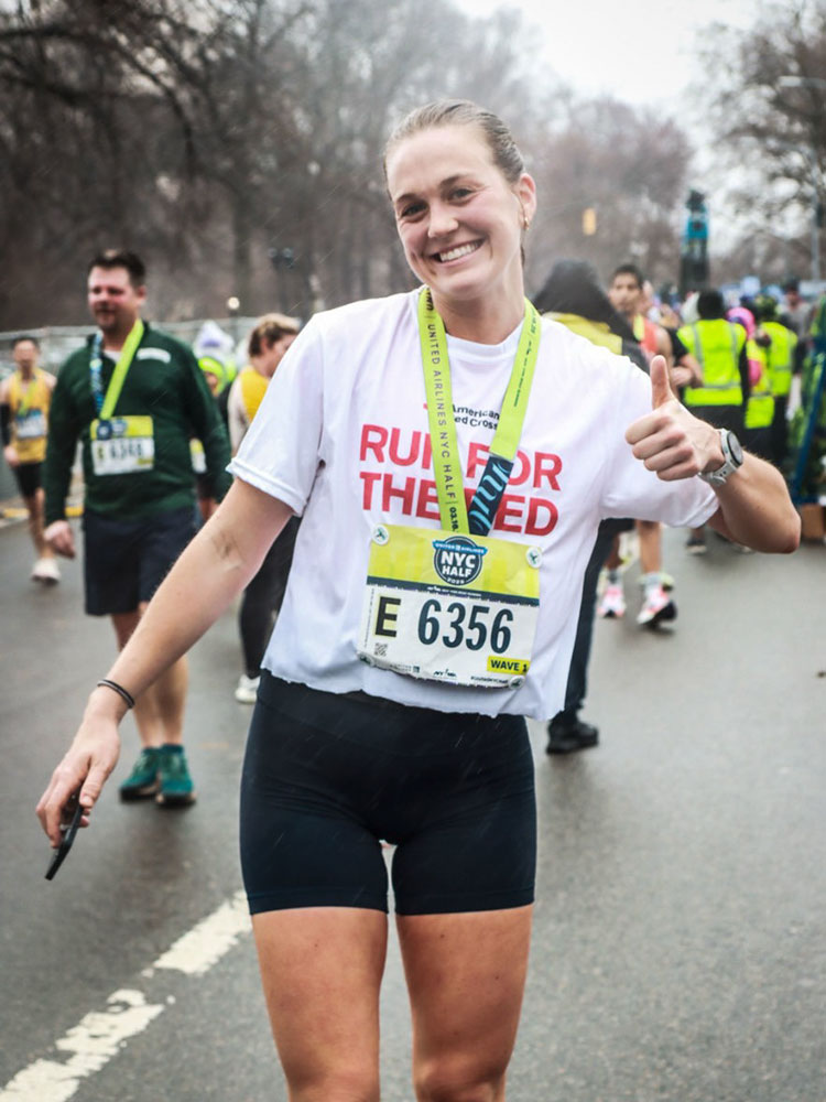 Kelly Van Hoesen running in a marathon and giving a thumbs up.