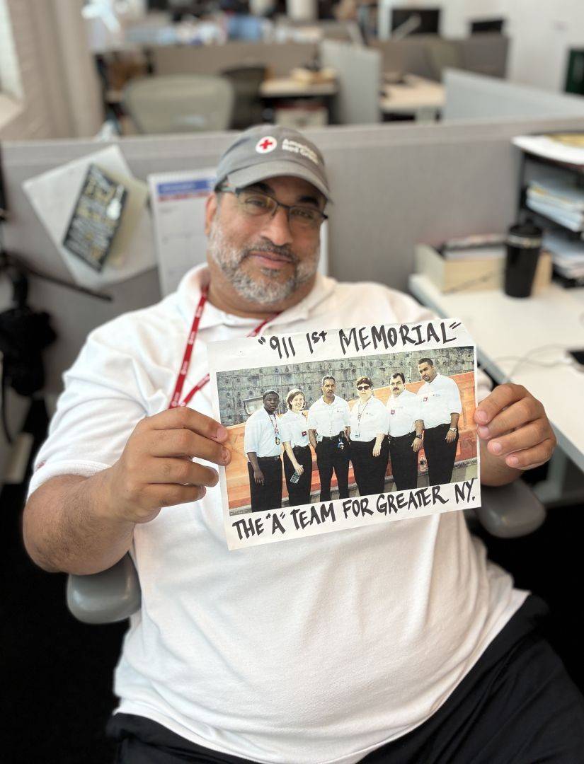 Person seated at a desk holding a photograph labeled “911 1st Memorial” showing a group of Red Cross colleagues.