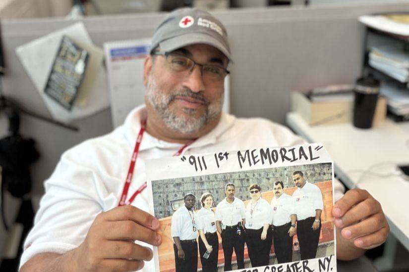 Person seated at a desk holding a photograph labeled “911 1st Memorial” showing a group of Red Cross colleagues.