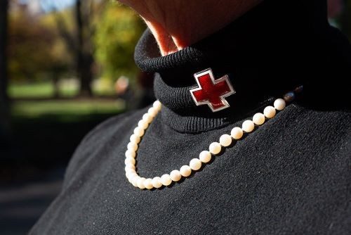 Close up image of Red Cross pin on turtleneck sweater with pearl necklace