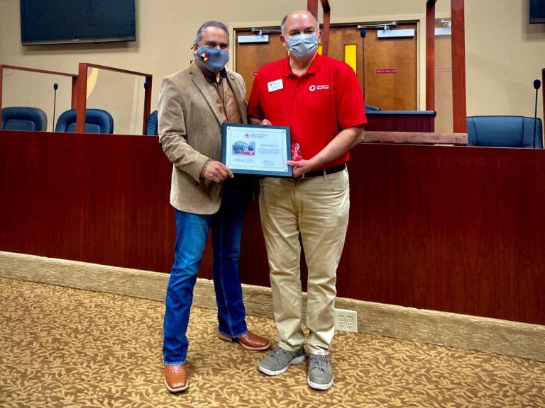 Two men stand holding award between them