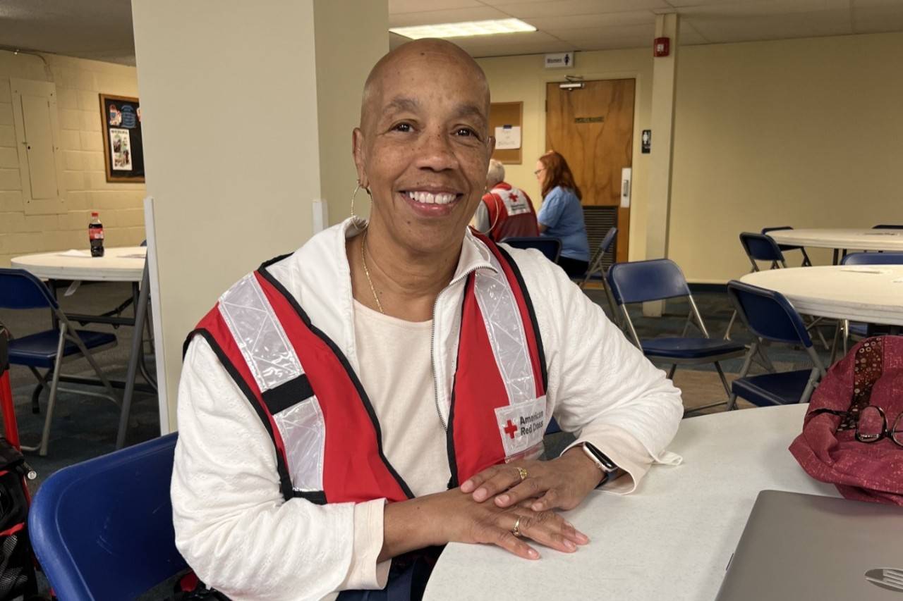 Woman sits at table wearing Red Cross vest
