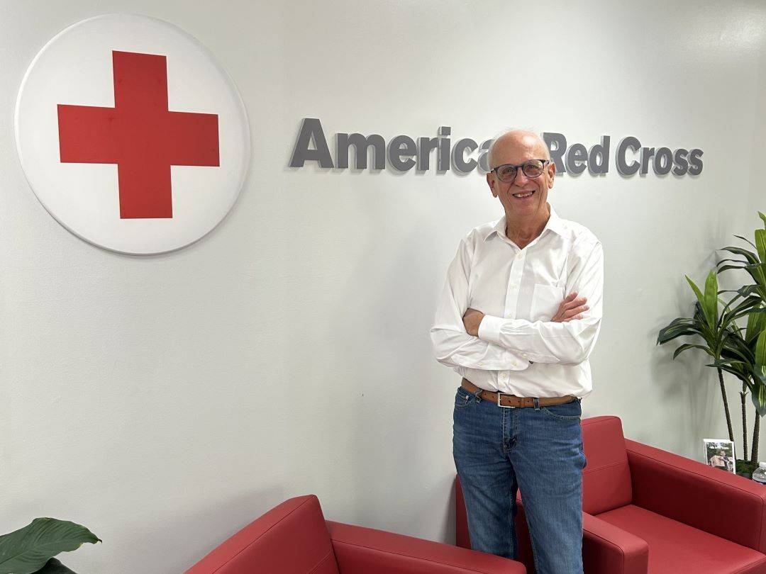 Man stands with arms crossed in front of American Red Cross sign