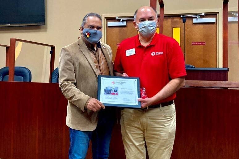 Two men stand holding award between them