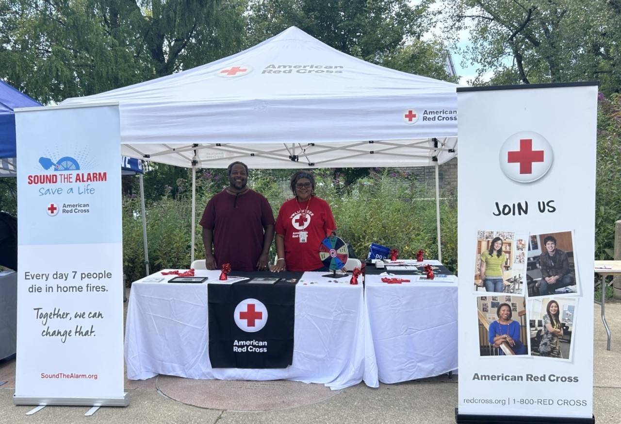 Two Red Cross volunteers standing at a tabling event behind a table