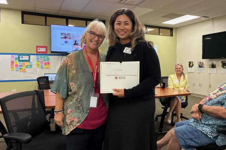 Two women stand side by side holding folder with Red Cross logo