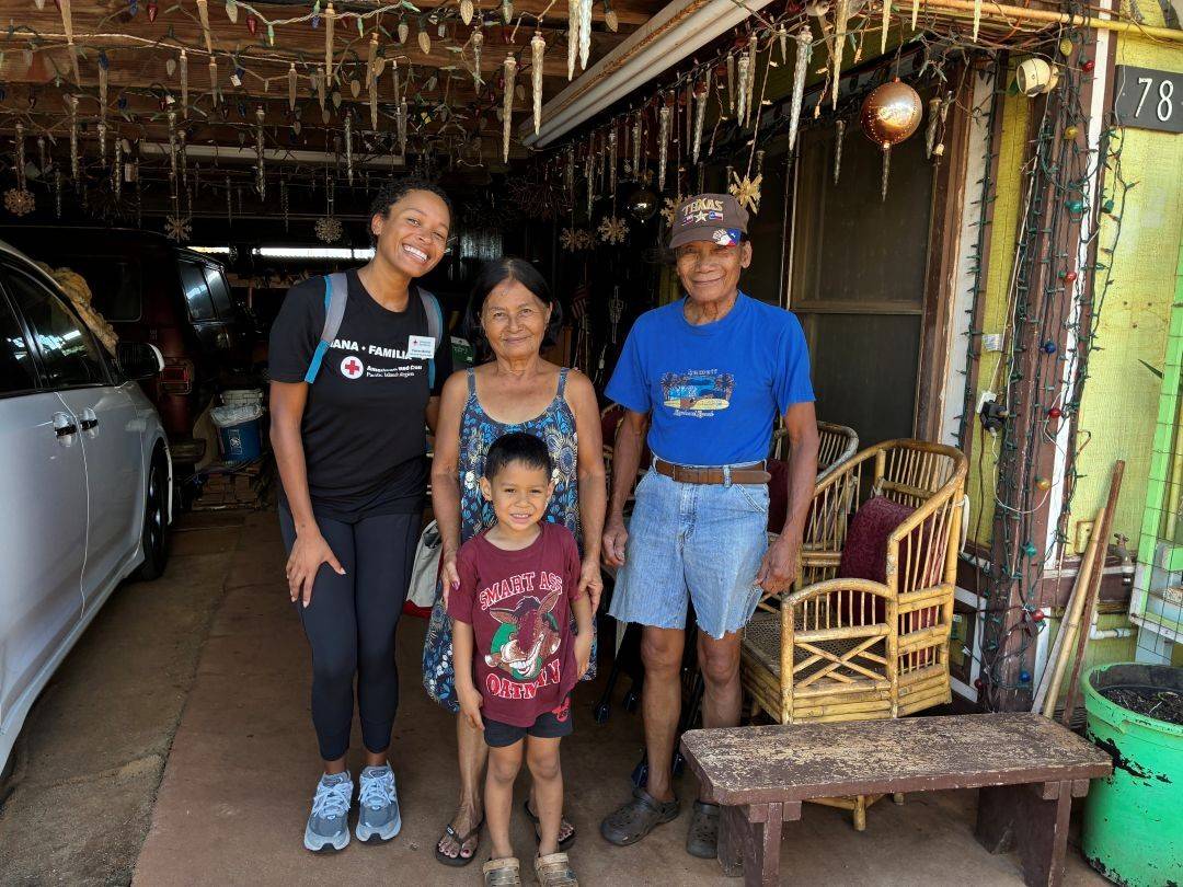 Red Crosser Pawnee Maiden stands inside garage with man, woman and child after installing their smoke alarms.