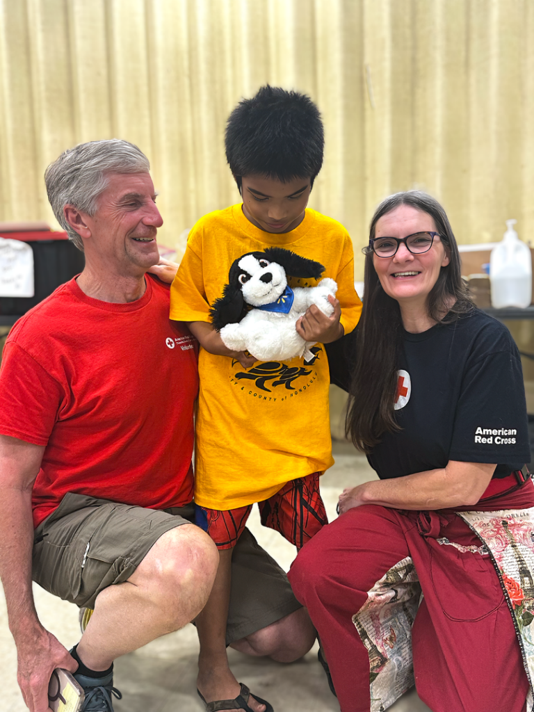 Two Red Cross volunteers kneel with young boy holding stuffed animal