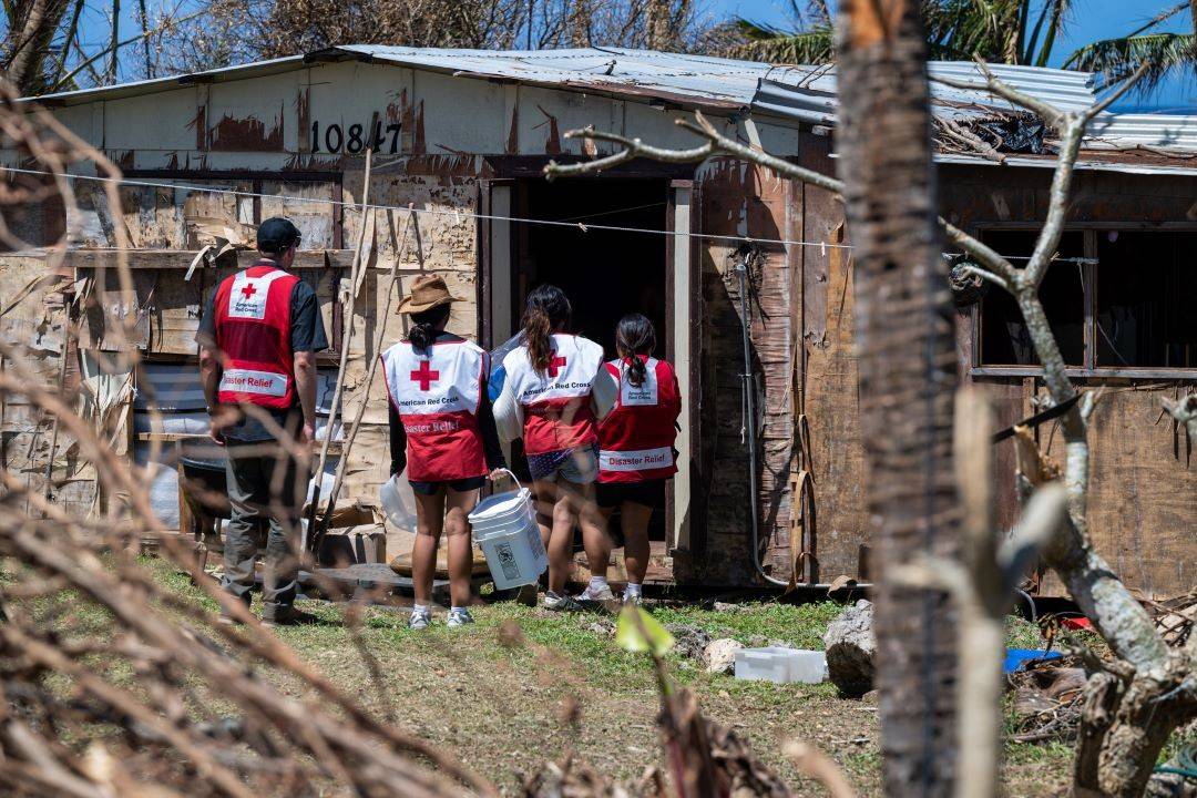 Group of Red Cross volunteers stand outside damaged home