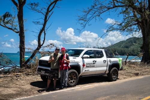 Two people stand in front of Red Cross truck